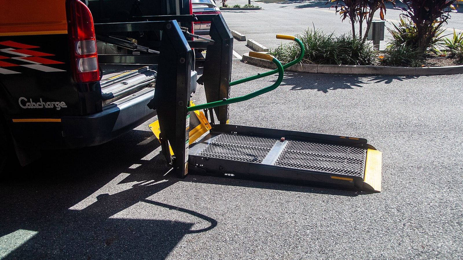 A wheelchair-accessible taxi with its hydraulic platform lowered to the ground.