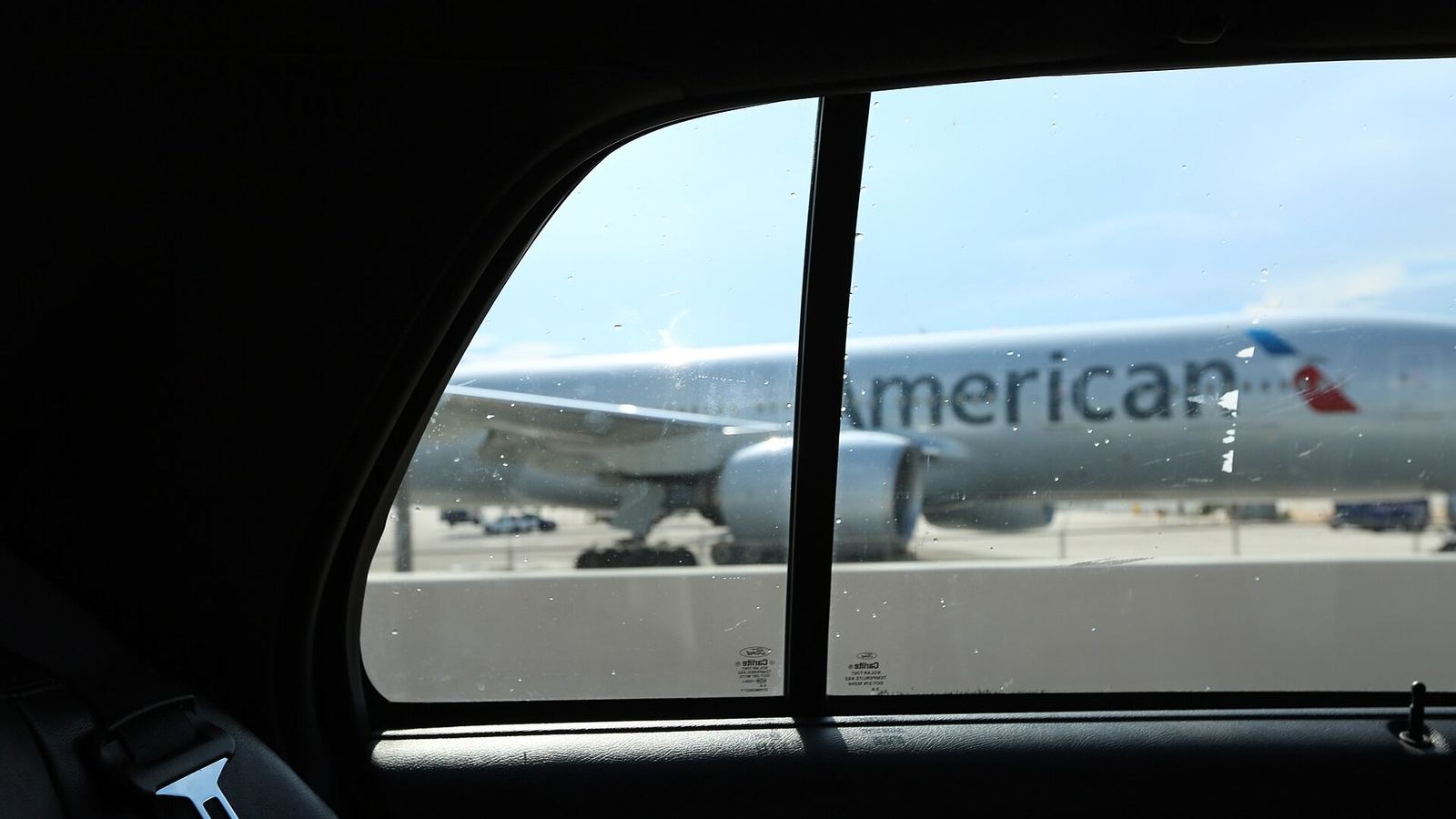 The view from a car's back seat towards an airliner parked beyond the window.