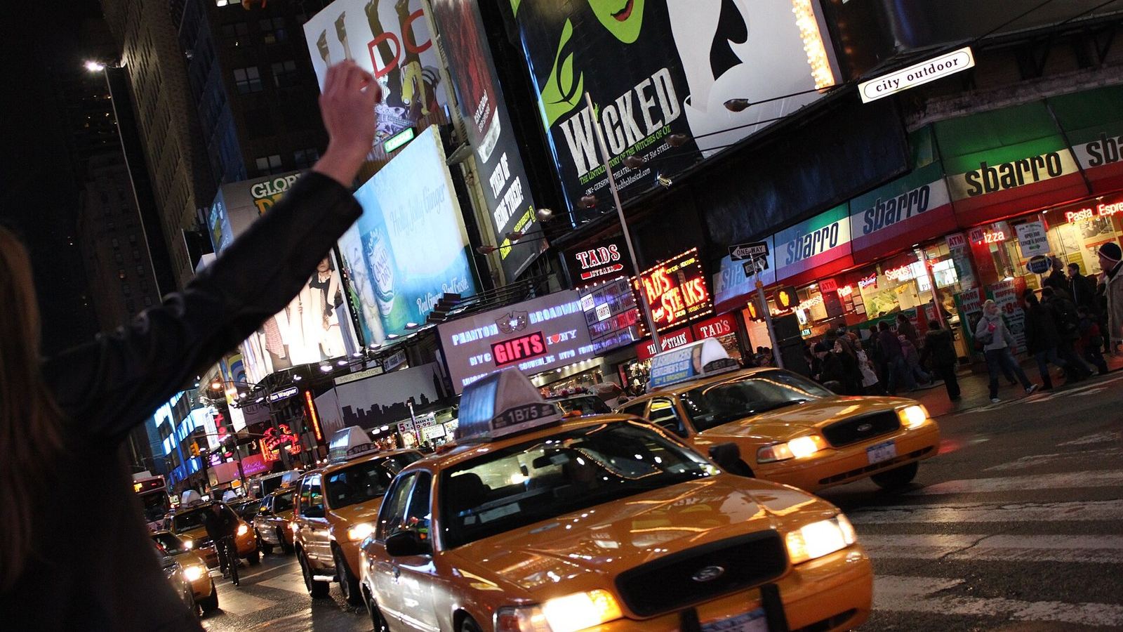 A raised arm hailing a yellow taxi at night in Times Square, New York.