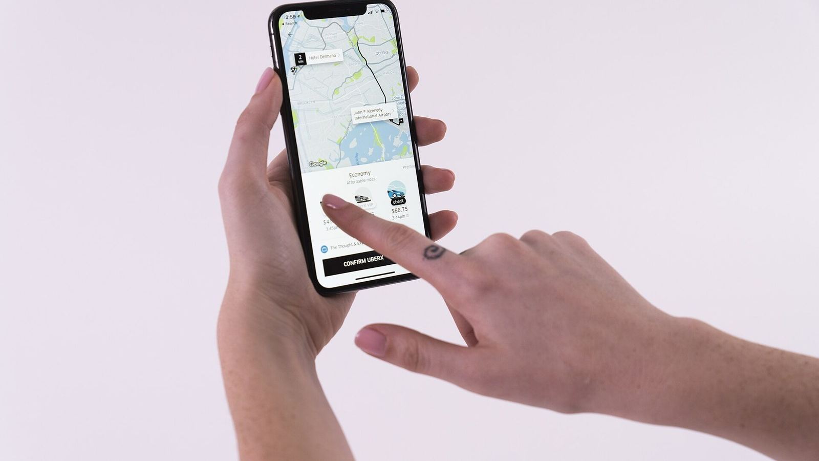 A hand holding a phone with the Uber app open on a map, a finger about to tap.