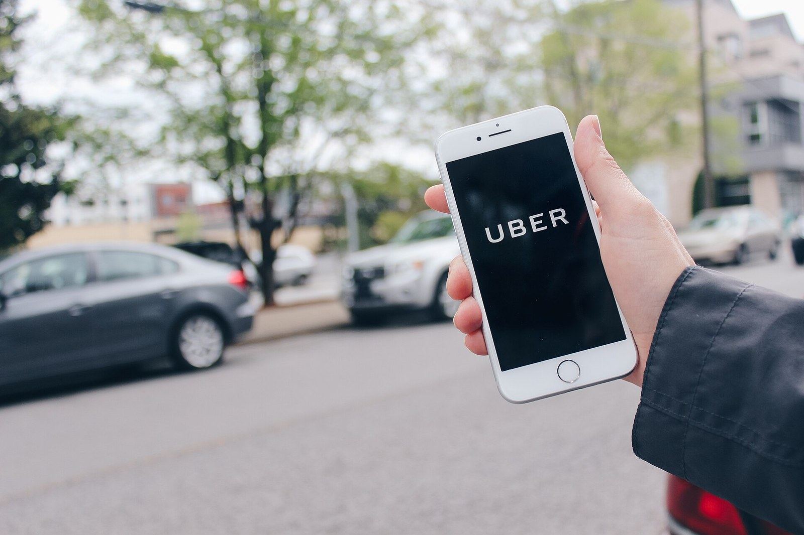 A hand holding a phone showing the Uber logo at the side of a street.