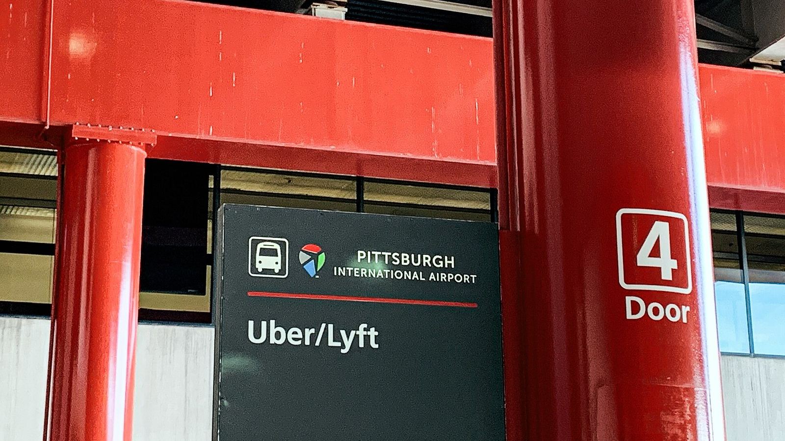 A sign at Pittsburgh International Airport pointing to the Uber and Lyft pickup area at door 4.